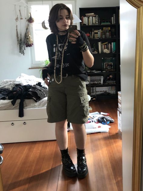 A mid-sized person/girl wearing a    black the cure shirt, green cargo shorts, fingerless gloves, platform dr. Martens and multiple dark green and gray crystal rings and bracelets. 		The person is also wearing multiple silver necklaces. Eco Goth Fashion, Summer Goth Masc, Alt Button Up Shirt Outfit, Eco Punk Fashion, Masc Skirt Outfit, Lillie Core, Masc Fairy Grunge Outfit, Masc Summer Outfits For Women, Adrogonus Outfits