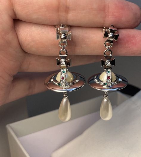 This item is pre-owned in a great condition, like new. Please do not purchase if this will bother you.  Revisiting Vivienne Westwood's iconic collection, dating back decades indulge in the glamorous and instantly recognisable Pearl Drop Earrings. Detailed with signature Westwood Orb beautifully adorned with multi coloured Swarovski crystals, the earrings are finished with a sophisticated pearl drop, perfected in silver-tone plated brass. Earring measurements: approx drop 5.5cm. Orb is approx 2.5cm W,2.5cm H. Come with Vivienne Westwood dustbag:) Vivienne Westwood Dangle Earrings, Vivienne Westwood Drop Earrings, Vivienne Westwood Ariella Earrings, Vivienne Westwood Wedding Ring, Aesthetic Vivienne Westwood, Vivienne Westwood Earrings, Vivienne Westwood Jewellery, Brass Earring, Jewelry Lookbook