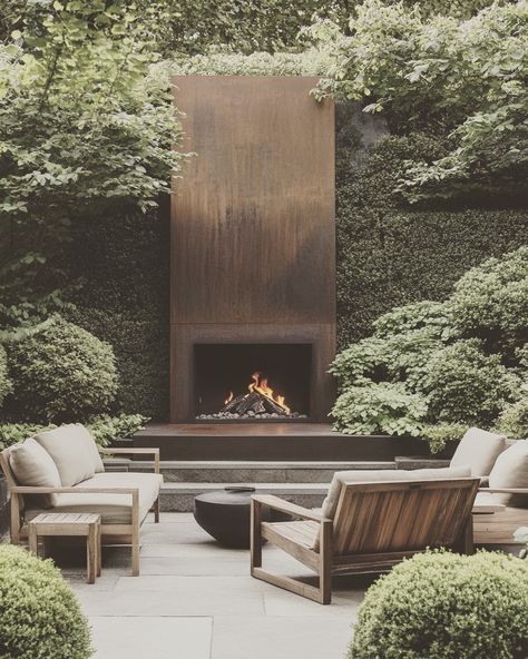 The corten steel minimalist fireplace🔥 adds a touch of timeless luxury to the backyard. Thoughtfully arranged greenery creates a private, enclosed space perfect for long conversations in the evening. The low-to-the-ground seating invites relaxation and enhances comfort, making it an ideal setting for unwinding with friends. #CortenSteel #MinimalistDesign #BackyardInspiration #OutdoorLiving #LuxuryOutdoorSpaces, #GardenDesign #FireplaceDesign #CozyVibes #RelaxationSpace #PrivateRetreat #Comfo... Corten Steel Fireplace Outdoor, Steel Outdoor Fireplace, London Fireplace, Ground Seating, Small Apartment Garden, Hill Villa, Reno House, Luxury Outdoor Spaces, Garden Fireplace