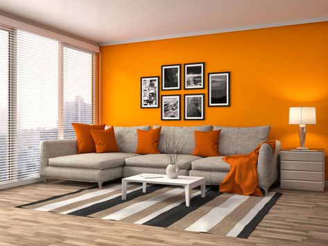 Orange never fails to give life to a dim and lonely living room. The wall in bright and cheerful orange is supported with the orange throw pillows and orange cloth resting on the sofa. Orange Painted Walls Living Room, Wall Color Ideas Orange, Orange Wall Living Room Ideas, Bright Orange Living Room, Orange Sofa Wall Color, Orange White Living Room, Bright Wall Colors For Living Room, Orange In Interior Design, Orange Wall Design Interiors