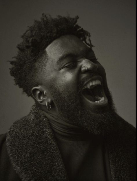 It is a black and white toned picture of black male with black hair that is shaved on the sides and longer on top, creating a crown of curls. He also has a beard that ends near the middle of his neck. He is wearing a turtleneck and vest; the picture is only from the shoulders up. He is also wearing dark hoops for earrings and a nose ring. His teeth are fanged and bared as if he is showing them of. End ID Black Vampire, Human Reference, World Of Darkness, Human Poses Reference, Arte Inspo, Human Poses, Anatomy Reference, Foto Inspiration, Art Poses