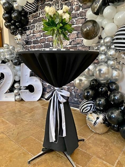 It is ideal to use high-end black spandex cocktail table covers for your upcoming birthday celebration as they are both durable and reasonably priced. To create a gentler look, put in some realistic cream roses in transparent glass vases. Decorate the space with a brown brick wall background to create a rustic vibe for your guests. Accessorize with black white and silver metallic balloon arch party kit that will uplift the venue. Make use of cordless LED number lights to provide subtle elegance Black And White Event Space, Cream And Black Party Decor, Brown Brick Wall, Number Lights, Event Decor Ideas, Party Decorations Table, Light Party, Brown Brick, Party Setup