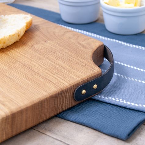 A rustic live edge solid Oak chopping board with a leather corner handle. Each wooden board is made to order and features a wonderful natural edge, making it a great gift for birthdays, weddings or as a gift for a loved one! Our boards are available in two sizes; medium (36x18-21cm) and large (40x21-24cm). Our chopping boards are proudly designed and handmade with care in our Edinburgh based studio, using the finest sustainable oak. We craft each board with long-standing, traditional wood workin Handmade Chopping Board, Chopping Board Aesthetic, Timber Chopping Boards, Cheese Board With Handles, Dinner On The Go, Oak Chopping Board Handmade, Oak Chopping Board, Bread Boards, Chopping Boards