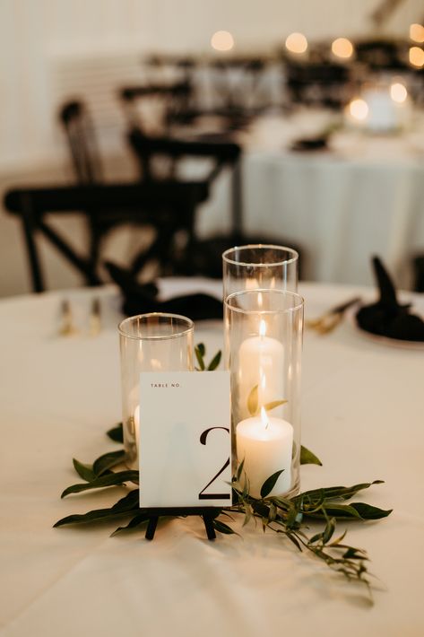 A romantic grouping of hurricane candles on top of  sprigs of greenery is a perfect touch to this elegant and modern wedding reception.

- Olivia Doerfler Photography Winter Wedding Simple Centerpieces, 3 Candle Centerpiece, Simplistic Table Decor Wedding, Candle Center Piece For Wedding Tables, Greenery For Wedding Tables, Simple Wedding Table Decor Candles, Simple Greenery Wedding Decor, Modern Simple Wedding Decor, Nonfloral Centerpiece Ideas Wedding