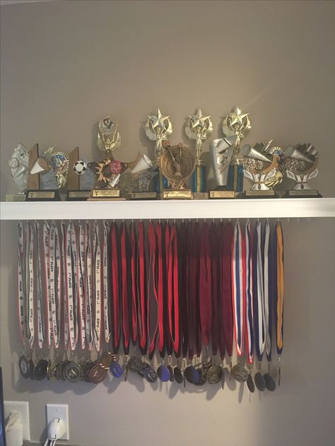 Medal and trophy display. Trophy Stand Design, Football Medal Display Ideas, Medals And Trophy Display Ideas, Trophy Storage Ideas, Trophy Organization Ideas, Cheer Trophy Display Ideas, Trophies And Medals Aesthetic, Dance Trophy Display Ideas, Medal And Trophy Display Ideas