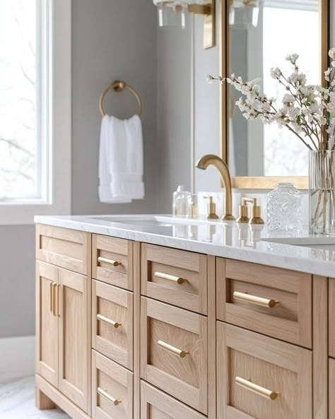 When it comes to creating a space that feels luxurious yet grounded, I love mixing natural tones and textures with sleek, modern fixtures. The oak cabinetry paired with the marble countertops and gold accents here creates that perfect balance of warmth and elegance, don’t you think? I’ve been obsessed with how the natural wood grains pop against the soft grey walls. And who knew a simple touch like fresh florals could transform the entire room? ⁣ ⁣ I’ve found that bringing in natural material... Master Bath Ideas Painted Cabinets, Light Wood And Gold Bathroom, Gold Hardware Cabinets, Guest Bath Double Vanity, Natural Wood Bathroom Vanity Master Bath, Beige And Wood Bathroom Ideas, Bathroom With White Oak Cabinets, Modern Oak Bathroom, Bathroom Light Wood Vanity