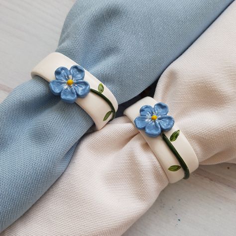 Handmade forget me not flower napkin ring for a rustic floral table setting. These elegant hand-painted unique floral napkin holders with blue flowers will be your eye-catching accessory at your farmhouse dinner party or wedding table. After painting the rings I made from white concrete with non-toxic water-based paint, I reveal the forget-me-not flower that I shaped by hand with ceramic clay. I hope it will make you and your loved ones happy with its unique and minimal appearance. For yourself Handmade Ceramic Napkin Holder, Napkins Rings Ideas, Polymer Clay Napkin Rings, Air Dry Clay Napkin Rings, Pottery Napkin Rings, Clay Napkin Holder, Napkin Holder Ideas, Clay Napkin Rings, Napkin Flowers