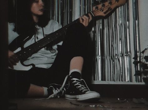 Girl sat on the floor holding bass guitar (black and white) wearing a black and white hoodie, black ghost necklace, black pants, white socks and converse, back ground is white wall with silver party curtain Grunge Bass Aesthetic, Male Bassist Aesthetic, Bassist Aesthetic Girl, Female Bassist Aesthetic, Bass Girl Aesthetic, Dark Guitar Aesthetic, Male Guitarist Aesthetic, Bass Player Aesthetic, Aesthetic Bass Guitar