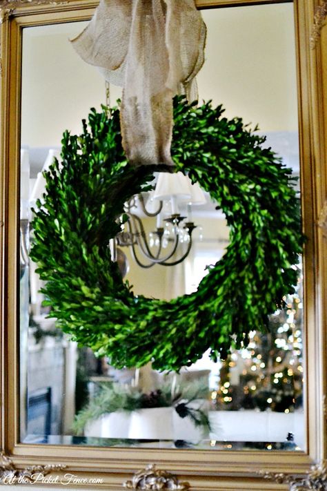 boxwood wreath hanging on mirror with burlap ribbon atthepicketfence.com Wreaths For Mirror, Wreath Hanging From Ribbon On Mirror, Christmas Wreath On Mirror, Wreath Over Mirror, Wreath On Mirror, Mirror Wreath, Boxwood Wreath Decor, Staircase Christmas, Mantle Wreath