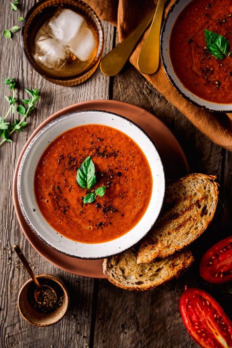 Overhead of Roasted tomato soup in a bowl topped with basil, pepper and served with grilled bread