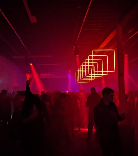 Photo of a darkened crowd in a warehouse made into an event venue lit by a line of square red lights Cyberpunk Bar, Warehouse Rave, Madison + Core + Aesthetic, Environment References, Warehouse Club, Peggy Guggenheim, Red Light District, Event Lighting, Event Inspiration