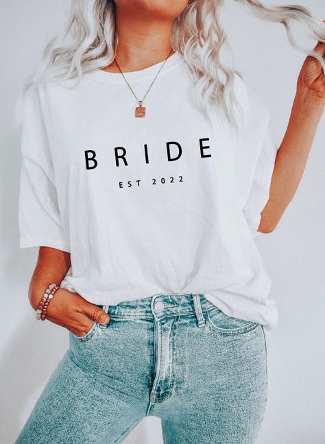 Elevate your bridal style with our Custom Bride Est 2022 T-shirt! Tailored to perfection, it's the perfect gift for every bride-to-be. Crafted with love, it exudes elegance and timeless charm. Embrace your unique journey with this stunning tee that captures the essence of your special day. Stand out and make a statement as you walk down the aisle. A must-have addition to your wedding wardrobe. Shine and create unforgettable memories in style. #BrideToBe #WeddingStyle #UniqueBride Bride Tshirt Ideas, Bride Shirt Ideas, Wedding Weekend Outfits, Gifts For New Grandma, Bridesmaid Tshirts, Personalized Bachelorette, Bride Shirt, Bridal Party Shirts, New Grandma