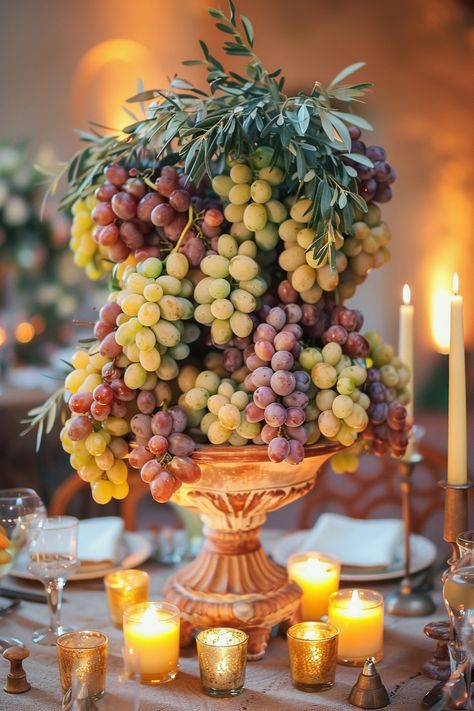 ✨ Elevate your wedding ambiance with a centerpiece that whisks you away to the rolling hills of Tuscany. Experience the charm of Italy as grape vines & olive branches intertwine with the warm glow of candles on your special day. #WeddingInspiration #TuscanWedding #RomanticDecor #WeddingIdeas #CountryChic #RusticElegance #GrapeAndOlive #CandlelightMagic Let the light guide your love story. Tuscany Rehearsal Dinner, Olive Branches Decor, Greek Tablescape, Round Tablescapes Wedding, Roman Feast, Roman Wedding, Wedding Table Deco, Ancient Vase, Wedding Ambiance