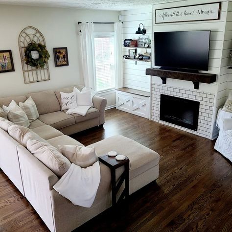 This beige chaise lounge sectional is seated on gorgeous dark wood living room flooring. The sectional faces a white subway tile fireplace fitted into a white shiplap wall. Complement the dark floors with a dark wood mantel mounted above the fireplace. Sofas For Dark Floors, Boho Living Room With Dark Floors, Dark Wood Floor White Walls Living Room, Living Room Furniture With Dark Floors, Modern Living Room With Dark Wood Floors, Wood Floor Furniture Living Rooms, Cozy Living Room Dark Floors, Living Room Paint Color Ideas Dark Floor, Living Room Ideas With Dark Floors