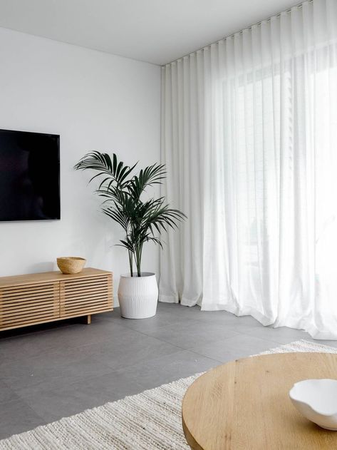 Dark and dull grey living area transformed into a warm and inviting space. The white linen sher curtains, oak side table, seagrass pouf, soft ivory rug, oak entertainment unit and indoor palm tree balance the cold of the grey floor tiles. Click now to see more photos of this beautiful living room Grey Tiles Living Room, Grey Flooring Living Room, Sheers Curtains Living Room, Flooring Living Room, Lounge Room Styling, Tiles Living Room, Grey Floor, Living Room Tiles, Room Styling