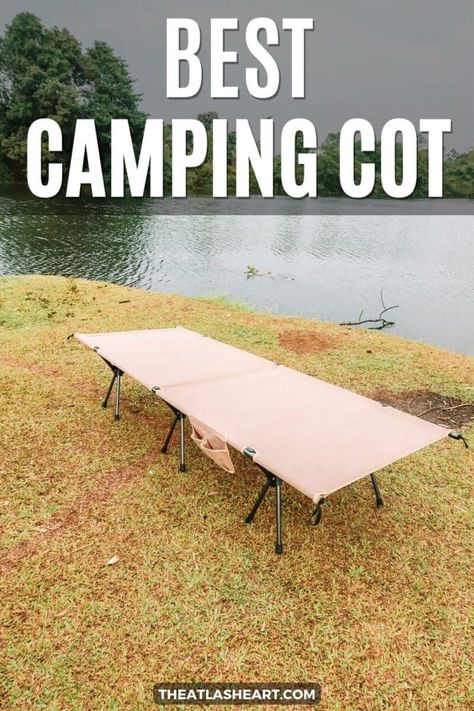 A beige canvas cot sits on a grassy bank of a greenish lake, with trees and an overcast sky in the background, with the text overlay, "Best Camping Cot." Camping Cot Ideas, Cot Ideas, Camping Cot Bed, Camping Cots, Essential Camping Gear, Sleeping Cots, Adventure Essentials, Camping Cot, Family Tent Camping