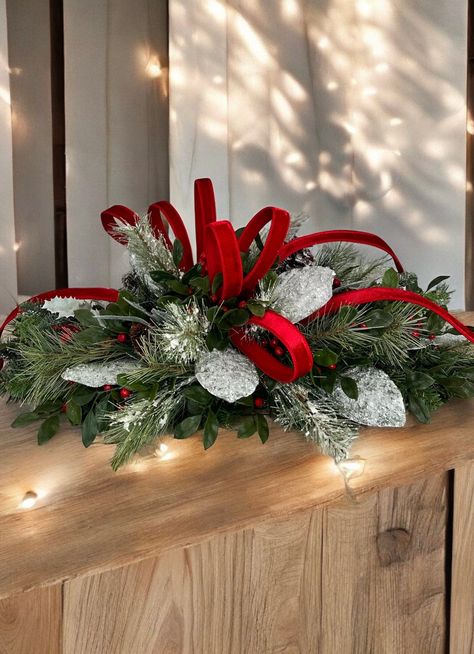 Add classic holiday elegance to your home with this traditional red and green Christmas centerpiece. Measuring approximately 30x21 inches, this handcrafted arrangement is perfect for creating a warm and festive atmosphere on your dining table, mantel, or entryway. The centerpiece features lush evergreen branches accented with frosted greenery, vibrant red berries, and sparkling silver magnolia leaves. The focal point is a stunning red velvet ribbon that weaves through the arrangement, adding a luxurious touch to this timeless decor piece. Ideal for holiday dinners, family gatherings, or simply to enhance your Christmas decor, this centerpiece embodies the beauty and tradition of the season. Its versatile design complements a variety of holiday themes, from classic to contemporary. Key Feat Natal, Christmas Table Decor Ideas 2024, Christmas Dining Table Centerpiece, Poinsettia Arrangement, Traditional Red And Green Christmas, Christmas Floral Arrangements Diy, Dinners Family, Christmas Arrangements Centerpieces, Christmas Floral Designs