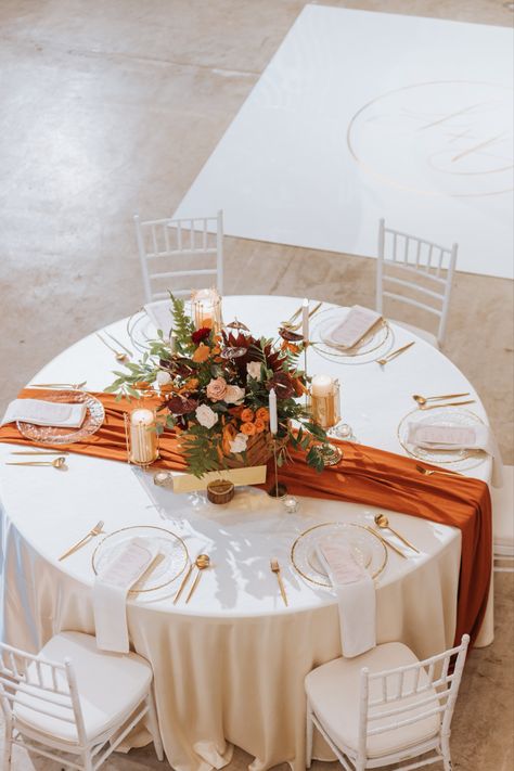 Main wedding table with burnt orange table runner. Decorated with a floral centerpiece alongside candles and furnished with glassware. Wedding Decor Terracotta, Main Wedding Table, Terracotta Wedding Bridesmaid Dresses, Orange Dress Outfit Wedding, Bridesmaid Dresses Burnt Orange, Burnt Orange Table Runner, Copper Saree, Orange Wedding Decorations, Summer Sandals For Women