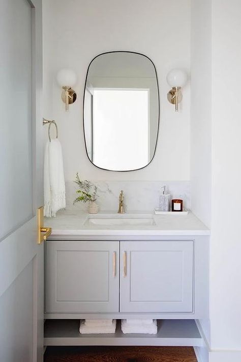 Powder room features a black oblong mirror flanked by brass and glass globe sconces over a gray washstand with a honed white marble countertop and a gray door. Oval Mirror Bathroom, Capsule Design, Deep Frame, Transitional Bathroom, Contemporary Mirror, Ensuite Bathroom, White Marble Countertops, Blue Bathroom, Oval Mirror