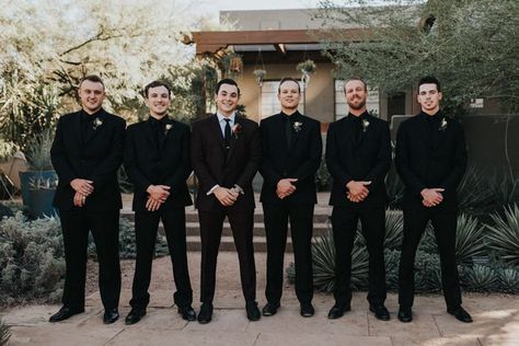 This Black, Burgundy, and Gold Desert Botanical Garden Wedding is a Total Showstopper All Black Groomsmen Attire Wedding, Black On Black Mens Wedding Suit, Groomsmen In All Black Suits, Groomsmen Black On Black, Black And Gold Bridal Party Attire, Fall Wedding Groomsmen Attire Black, Blacked Out Groomsmen, Black White And Green Wedding Groomsmen, Groomsmen All Black Suit