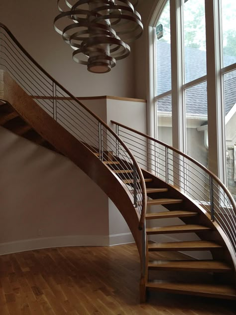 Sleek and modern wooden curved staircase with cable railings. Open Riser Stairs, درابزين السلم, Round Stairs, Curved Stairs, Steel Railing Design, Circular Stairs, Concrete Staircase, Staircase Design Modern, Staircase Railing Design