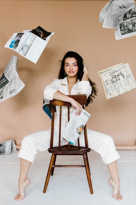 Female model in a cream Free People Utility Jumpsuit sitting on a backward chair with newspapers flying in the air. Newspaper Editorial, Newspaper Photo, Studio Photoshoot Ideas, Beautiful Photoshoot Ideas, Brand Photography Inspiration, Studio Photography Poses, Utility Jumpsuit, Business Photoshoot, Branding Photoshoot Inspiration