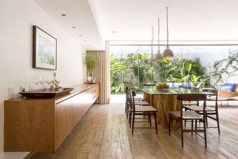 Dining Room, Chair, Table, Medium Hardwood Floor, Pendant Lighting, Rug Floor, Bar, and Recessed Lighting "We maximized natural lighting, ventilation, and contact with the outdoors in all environments, which sometimes open onto the street at the height of the treetops, or opens onto an outdoor area with a tropical garden," explains the architects.     Photo 7 of 13 in Lush Gardens Infuse Tropical Vibes in This Chic Brazilian Home Tropical Dining Room, Sala Grande, Inside Decor, Rooftop Patio, Patio Interior, Living And Dining Room, City House, Metal Furniture, Family House