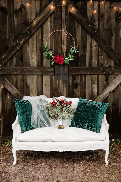 Rustic Christmas Inspired Wedding Decor, Wooden Barn Backdrop with White Vintage Loveseat with Green Pillows and Wedding Veil, Wedding Bouquet with Red Florals and Greenery, Hanging Gold Floral Hoop with Red Roses | Bushnell Florida Christmas Inspired Wedding, Red And Pink Wedding, Vintage Loveseat, Barn Backdrop, Christmas Wedding Themes, Christmas Wedding Decorations, Wooden Barn, Christmas Mini Sessions, December Wedding