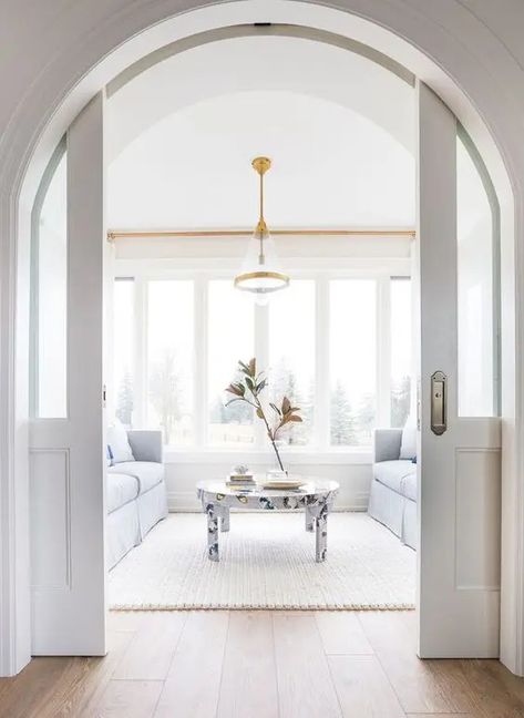 a light filled white living room with a glazed wall, pale blue sofas and a butterfly print table, white arched pocket doors Modern Farmhouse Ideas, Style Salon, Interior Design Per La Casa, Arched Doors, White Living, White Living Room, Design Del Prodotto, Decor Minimalist, Design Living Room