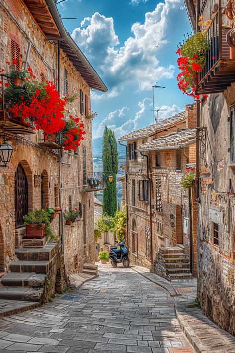 Cobblestoned street in San Gimignano, Italy with red flowers and vintage architecture under clear blue sky Italy Places Aesthetic, Italy Cobblestone Streets, Narrow Streets Italy, Italian Neighborhood Aesthetic, Old Italian Architecture, Italian Buildings Architecture, Streets In Italy, Italy Buildings, Architecture In Italy