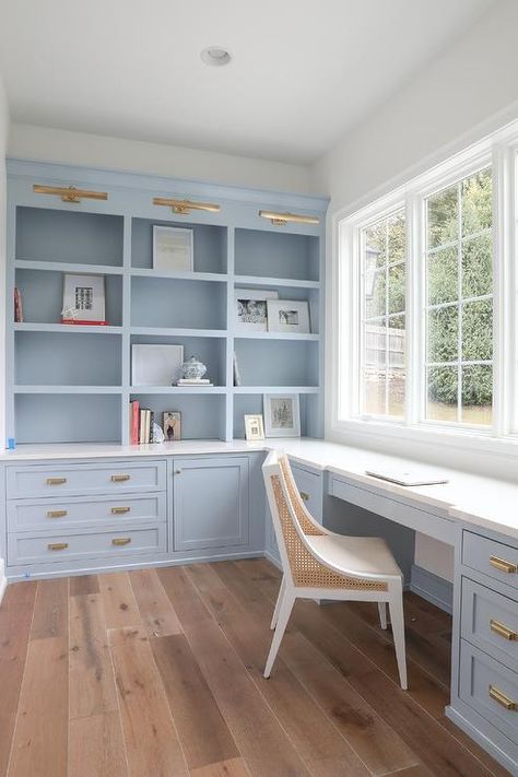 Office features blue built in desk and shelves, painted in Benjamin Moore Blue Heather semi-gloss, topped with honed white marble and vintage brass cup pulls, antique brass picture lights, and a white and tan cane desk chair. Bright Home Library Ideas, 8x8 Office, Benjamin Moore Blue Heather, Blue Built Ins, Playroom Sunroom, Built In Desk And Shelves, Den Library, Benjamin Moore Blue, Coastal Office