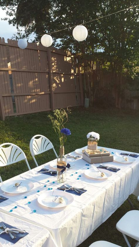 Navy blue graduation table setup outdoor backyard, white tablecloth, white chairs, white plates, gold ferrero rocher favors, wine bottle centerpieces with burlap, blue ribbon bow, twine, blue flower, baby's breath, rustic jar, white flower, white Chinese lanterns Navy Blue Grad Party, Navy Blue Graduation Party Decorations, Graduation Party Blue And White, Ferrero Rocher Favors, Light Blue Grad Party, Blue And White Graduation Party Ideas, White Chinese Lanterns, Blue Grad Party, Simple Party Table