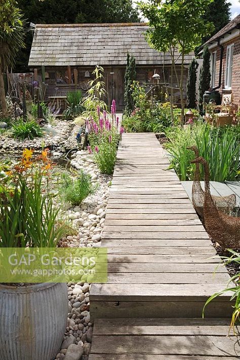 Seaside Inspired garden. Timber decking pathway through seaside garden leading to rustic beach hut. Crocosmia planted in old metal dolly tub, wirework geese sculptures, Lysimachia - Loosestrife and pebble beach. Decking Pathway Ideas, Deck Pathway Ideas, Beach Garden Ideas Coastal Style, Coastal Landscaping Ideas Beach Gardens, Beach Garden Ideas, Decking Path, Seaside Garden Ideas, Decking Pathway, Beach Cottage Garden