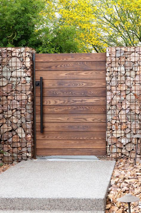 You can incorporate Thermory’s natural wood into your home in small ways. The gates in these photos are an example of small-scale biophilic design. Plus, using shorter boards is a great way to incorporate sustainable construction solutions. All doors were constructed by JD Stairs using 1 x 4 or 1 x 6 Thermory Benchmark Ash cladding in C20 profile. The horizontal fence material was cut down to a 1 x 3 out of 1 x 6 Benchmark Ash. You might want to think twice before tossing shorter board scraps! Gabion And Wood Fence, Stone And Wood Fence, Wooden Fences And Gates, Outdoor Fence Ideas, Modern Wood Gate, Modern Horizontal Fence, Natural Fences, Small Garden Gates, Backyard Fence Design