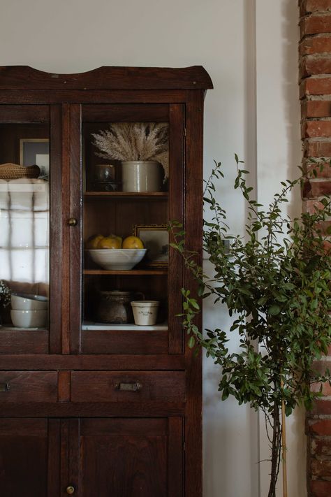 Rustic dark wood hutch shelf decor. Antique hutch decor. Antique hutch interior shelves. Shelf styling inspiration and ideas. Earthy toned decor. Vintage glassware, antique pottery, sketch art, and handmade dinnerware for kitchen shelf decor. Styling inspired by Amber Interiors - styled by Nadine Stay. #shelfdecor #shelfie #hutchdecor #hutchstyling #kitchenpantry #vintageglassware #handmadepottery #shelfstyling Vintage Hutch Decorating Ideas, Dining Hutch Styling, Dining Room Hutch Antique, Rustic Glass Cabinet, Dining Room Hutch Ideas, Hutch Decorating Ideas, Litchen Hutch, Kitchen Hutch Decor, Bar Hutch