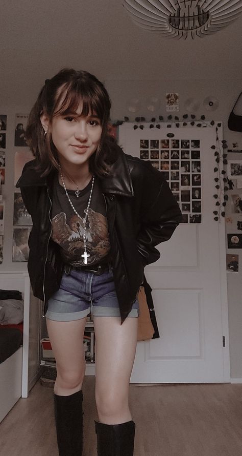 A girl standing in her room in shorts, a queen T-shirt, leather jacked, leather boots and a white cross-neckless 50s Fashion Rock N Roll, 90 Rock Outfit, Outfits For A Gig, Cool Rock Outfits, Old Rock Concert Outfit, Female Rockstar Outfit 80s, Rock Band T Shirts Outfits Women, 80s Rockstar Gf Outfits, 80s Rock Women Outfits