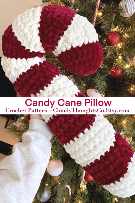 A hand holding an oversized crochet candy cane pillow in front of a Christmas tree. The  pillow is fluffy with burgundy and cream stripes. Crochet Candy Cane, Candy Cane Pillow, Crochet Candy, Crafts Cute, Winter Crochet, Crochet Decor, Crochet Xmas, Crochet Bedspread, Crochet Design Pattern