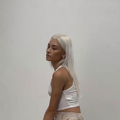 A photograph of a young Asian woman with tan skin and white hair, wearing a white cropped tank top. She faces three quarters left in front of a plain white background. Tan With Platinum Blonde Hair, Platinum Hair On Tan Skin, Platinum Blonde Tan Skin, Platinum Blonde Olive Skin, Platinum Hair Olive Skin, Platinum Blonde Hair On Tan Skin, Platinum Blonde Hair Tan Skin, Blond Hair Tan Skin, Tan Skin White Hair