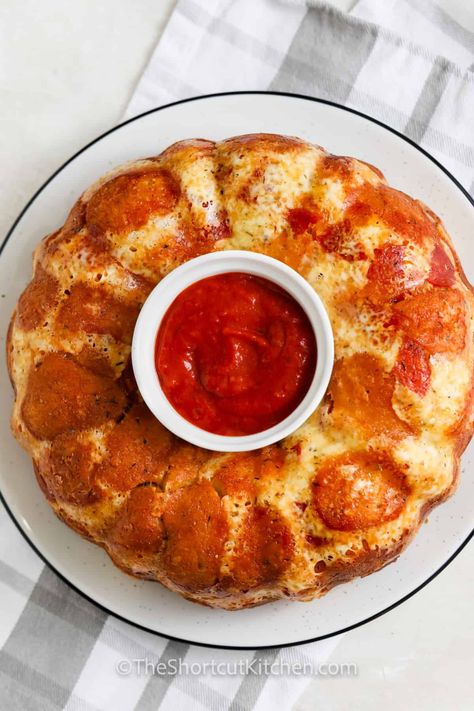 Kids always have a blast making pull apart pizza bread! Canned biscuit dough is cut it into quarters, and mixed with Italian herbs, garlic, pepperoni, mozzarella, and parmesan. Place the seasoned dough pieces into a bundt pan, and let the oven work its magic until it's fluffy and golden brown. Serve this crowd-pleaser with lots of pizza sauce for dipping! #pullapartpizzabread #pullapartbread #theshortcutkitchen #pizza pullapartbread Pizza Bundt Pan Pull Apart Biscuit, Pizza In Bundt Pan Pull Apart, Pepperoni Pull Apart Bread Bundt Pans, Bundt Pizza Pull Apart, Pizza In A Bundt Pan, Pizza Bundt Pan Pull Apart, Pull Apart Pizza Bread Bundt Pans, Bundt Pan Pizza Pull Apart, Savory Bundt Pan Recipes