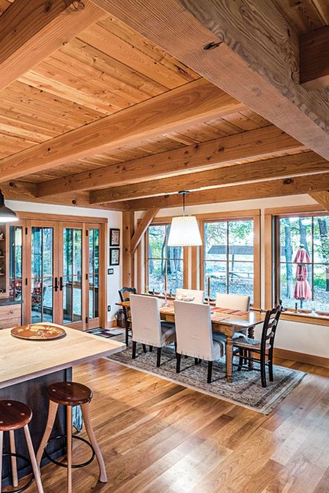 The connected open space on the 1,200 square-foot main level is filled with dining, living and kitchen areas. The Douglas fir posts and timbered ceilings establish a sense of contentment and comfort, while the abundant natural light gives it levity and space to breathe. The kitchen’s perimeter counters are capped with Corian while the center island is topped with silky maple. Photography by Scott Hemenway. Douglas Fir Walls, Douglas Fir Ceiling, Timber Frame House Interior, Timber Ceilings Interior, Timber Frame Interior Design, Timber Frame Home Interiors, Barndo Interior, Timber Frame Interior, Timber Interior