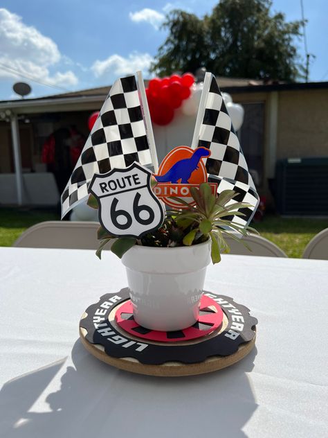 Potted succulents with race car flags and route 66 sign as a Cars theme centerpiece. Disney Cars Theme Centerpiece Ideas, Cars Disney Centerpieces, Racecar Theme Centerpieces, Racecar Party Centerpieces, Car Theme Centerpieces, Fast One Table Centerpiece, Nascar Centerpiece Ideas, Car Birthday Centerpieces, Car Party Centerpiece