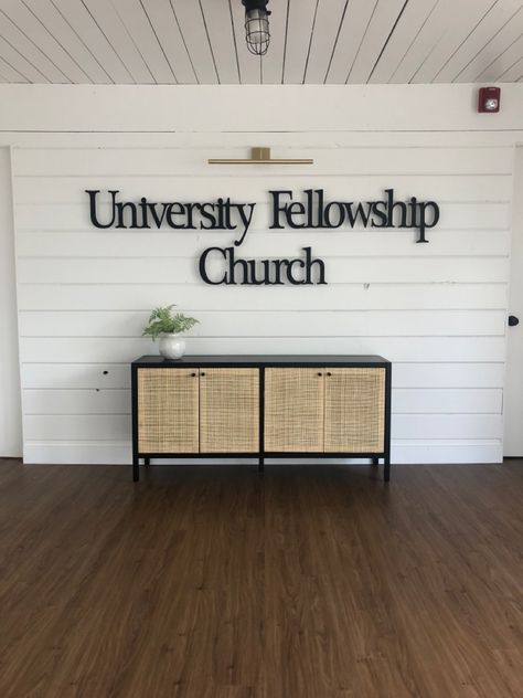 This church has a new brand wall in the entryway of their small event space. Black metal lettering, a library light and storage in their console table make this entryway inviting and functional! Church Foyer Decor, Church Lobby Design Foyers, Small Church Foyer, Church Entryway Decor, Church Foyer Ideas Lobbies, Small Church Stage Design, Small Event Space, Foyer Decor Entryway, Small Foyer Ideas