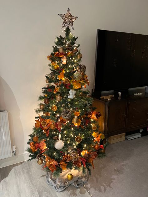 A dark green Christmas tree decorated with dehydrated orange slices, orange fall leaf garland, orange and brown baubles, acorns and red winter berries. On the top of the tree is a wicker star which also includes red winter berries. Throughout the whole tree are warm white lights giving a cozy vibe. Orange Baubles Christmas Tree, Copper Orange Christmas Tree, Orange Gold Christmas Tree, Orange Christmas Decorations Color, Orange Theme Christmas Tree, Orange And Brown Christmas Decor, Autumnal Christmas Tree, Orange And Red Christmas Tree, Orange And Green Christmas Tree