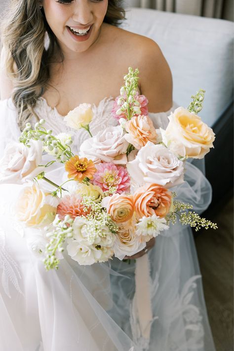 This romantic bridal bouquet was created for a bride and groom who got married this summer at Morgan's on Fulton. These soft, boho blooms were designed and provided by Romee Willow Florals, an artful and eco-friendly florist. Flowers used in this bouquet were blush ranunculus, light pink dahlias, peach roses, blush roses, white delphinium, orange zinnias, and more. We love this portrait of the bride and groom under the bride's veil! To see more photos by Rachael Kazmier, click the link. Floral Ceremony Backdrop, Dahlia Bridal Bouquet, Blush Ranunculus, White Delphinium, Dahlia Wedding Bouquets, Pastel Bridal Bouquet, Yellow Bridal Bouquets, Pink Dahlias, Yellow Wedding Bouquet