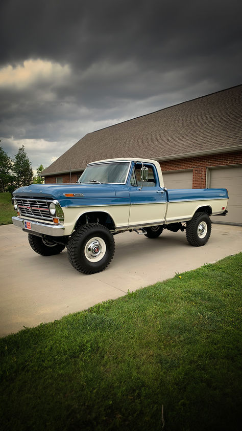 A beautifully maintained two-tone Ford Highboy pickup truck in blue and white, parked confidently on a concrete driveway. The towering stance of the truck is accentuated by large, robust tires and its classic design. Overcast skies loom above, suggesting an impending storm, yet the Highboy stands as a testament to the enduring strength and style of Ford's truck legacy. White Pickup Truck, Ford Highboy, American Pickup Trucks, 1979 Ford Truck, Bronco Truck, Country Trucks, Vintage Pickup, Custom Pickup Trucks, White Truck