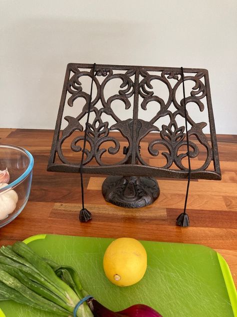 This is a stylish and ornate cook book stand for the kitchen. It is perfect for keeping your page whilst following a receipe. The stand is made from cast iron and has an elegant heart design. The receipe stand has a rustic brown finish with a tinge of black. Two weighted cords hold your page open. Measures: (h) 24 x (w) 26 x (d) 13 cm Cook Book Display Ideas, Cook Book Holder, Cookbook Display, Cottage Goth, Thrift Manifest, Goth Kitchen Decor, Recipe Book Stand, Cast Iron Kitchen, Thrift Wishlist