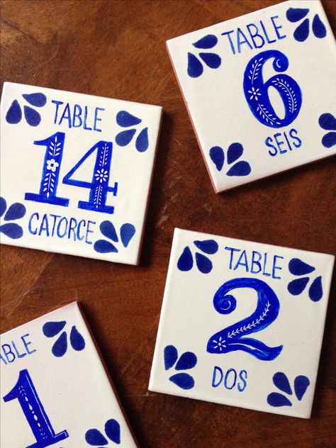 DIY Spanish tile table numbers for our wedding | Tiles ordered from Tierra Y Fuego. Painted with acrylic and design etched with cheap calligraphy pen nib. Spray with fixative to prevent scratching. Portugal Themed Party, Spanish Centerpieces, Tile Numbers Wedding, Diy Talavera Tiles, Portuguese Wedding Decor, Mexican Wedding Table Numbers, Mexican Table Numbers, Wedding Tiles, Tile Seating Chart Place Cards