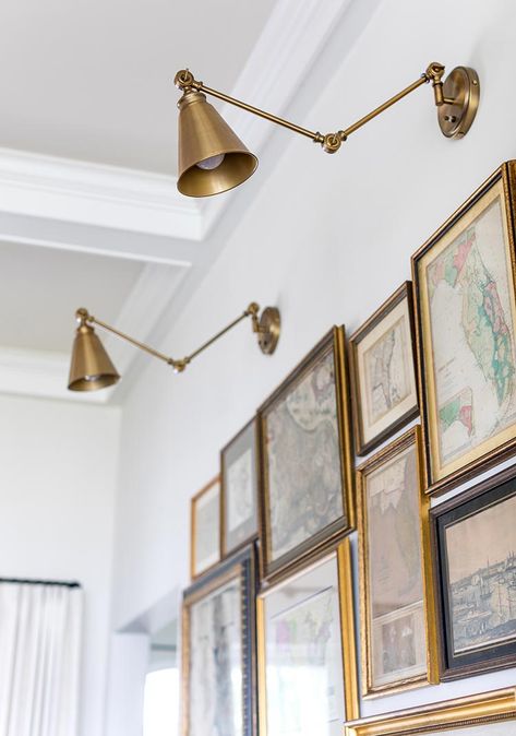 A gallery wall of vintage maps and other ephemera are hung close together. Overhead, two brass wall sconces shed light on the display. See more at cottagesandbungalowsmag.com Brass Photo Frame Wall, Vintage Map Gallery Wall, Library Wall Lights, Gallery Wall And Sconces, Wall Sconces Over Pictures, Sconces Above Pictures, Art Wall Lighting, Picture Light Sconces, Wall Art With Sconces Living Rooms