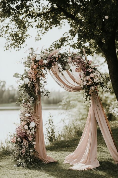 Floral wedding arch draped with blush fabric in an outdoor setting near a lake. Wedding Arches Diy, Boho Chic Wedding Decoration, Wedding Arch Decor Ideas, Arch Decor Ideas, Arch For Wedding Ceremony, Wedding Arch Decoration Ideas, Arch Decoration Ideas, Wedding Arch Decorations, Simple Wedding Arch