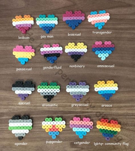 four by four rows of lgbtq+ flags made from perler beads in the shape of hearts on a wooden table as a background, from left to right these are the flags : lesbian, gay man, bisexual, transgender, pansexual, genderfluid, nonbinary, omnisexual, asexual, aromantic, greysexual, aroace, agender, pupgender, cat gender and the general lgbtq+ community flag. Cat Gender, Hama Art, Hamma Beads Ideas, Melty Bead Patterns, Easy Perler Beads Ideas, Fuse Bead Patterns, Diy Perler Bead Crafts, Perler Crafts, Pinterest Diy Crafts